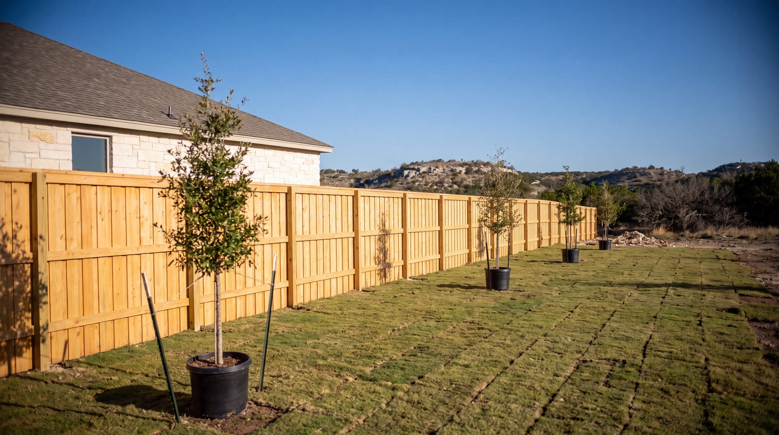 A new cedar board-on-board fence behind a just-finished Hill Country home