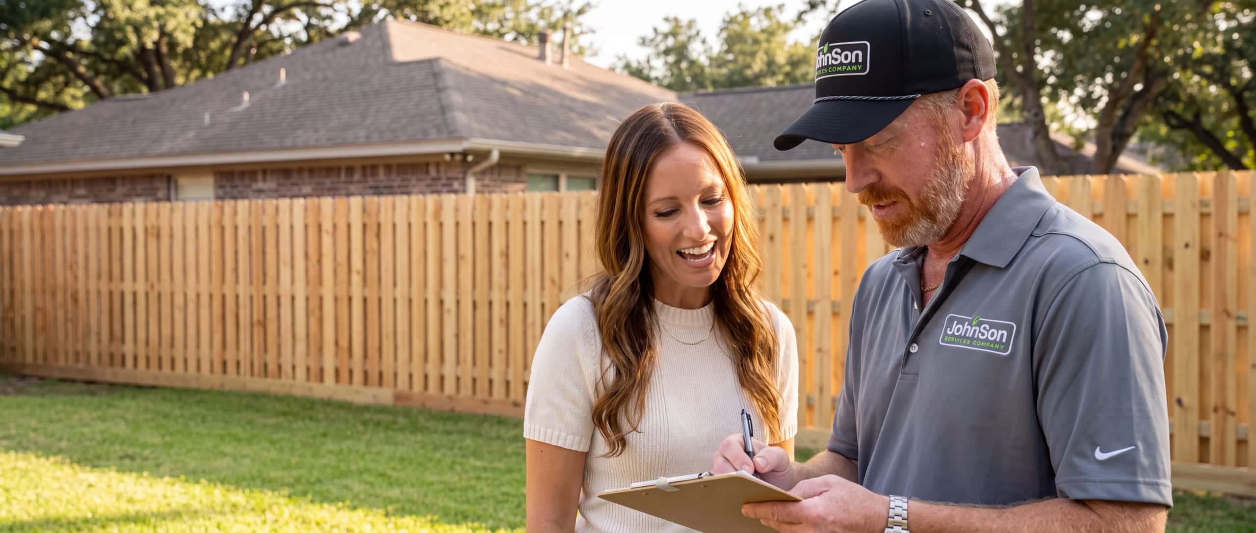 A Johnson estimator writing a fence quote on a clipboard beside a homeowner.